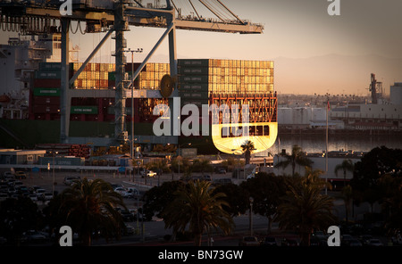 Port of Long Beach, Los Angeles, California at sunrise. Barge heavily loaded with Shipping Containers in morning sunlight. Stock Photo