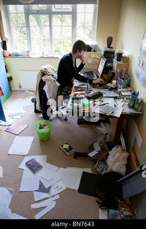 Teenager studying at a computer in a messy bedroom. Stock Photo