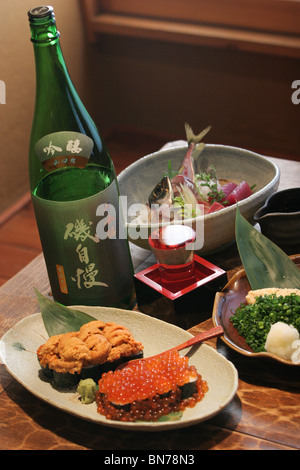 A plate of ikura (salmon eggs) and uni (sea urchin) , beside a bottle of sake in a Japanese restaurant Stock Photo