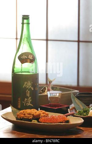 A plate of ikura (salmon eggs) and uni (sea urchin) , beside a bottle of sake in a Japanese restaurant Stock Photo