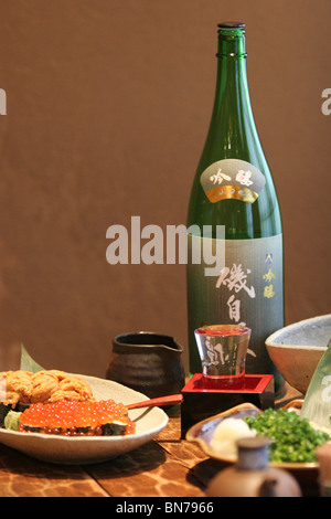 A plate of ikura (salmon eggs) and uni (sea urchin) , beside a bottle of sake in a Japanese restaurant Stock Photo