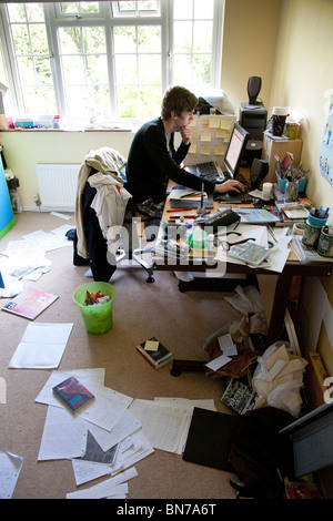 Teenager studying at a computer in a messy bedroom. Stock Photo
