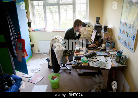 Teenager studying at a computer in a messy bedroom. Stock Photo