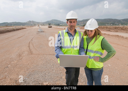 Hispanic construction workers using laptop in field Stock Photo