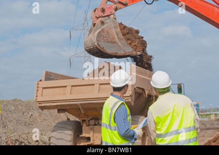 Hispanic construction workers watching dirt falling into dump truck Stock Photo