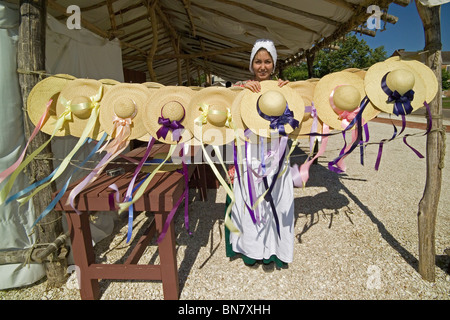 A costumed milliner sells ladies' straw hats with bows and ribbons at Market Square in historic Colonial Williamsburg in Virginia, USA. Stock Photo