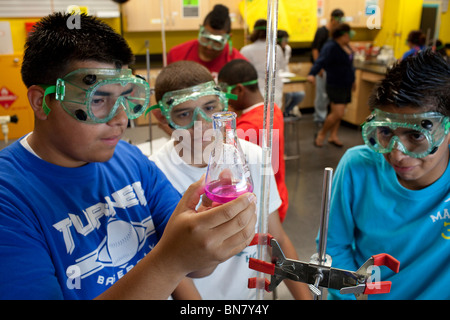 Hispanic high school boys in safety goggles look at solution in flask during titration experiment in chemistry class Stock Photo