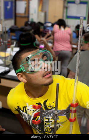 Hispanic male student wearing safety goggles watches solution in graduated cylinder during chemistry class Stock Photo