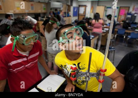 High school boys wearing safety goggles observe liquid in a graduated cylinder during a titration experiment in chemistry class Stock Photo