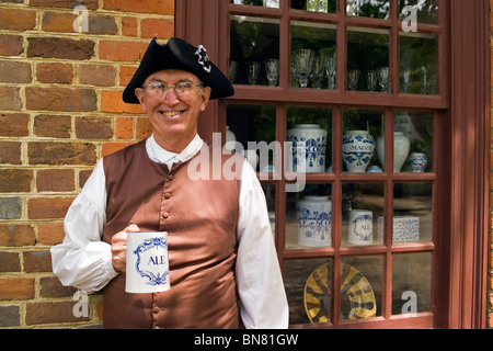 A merchant in his tricornered hat holds a ceramic ale mug, one of the 18th-century reproductions sold at shop in Colonial Williamsburg, Virginia, USA. Stock Photo