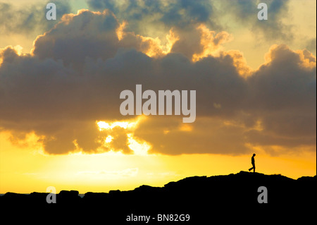 A silhouetted hiker walks along the cliff path at Godrevy beach in Cornwall Stock Photo