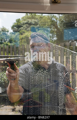 Window cleaner man cleaning outside windows wiping soap suds with squeegee seen through glass from inside Stock Photo