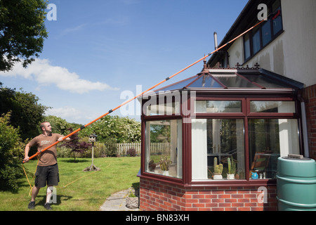 Window cleaner using a soapless pure water fed long pole and brush window cleaning system to clean residential house windows above a conservatory. UK Stock Photo