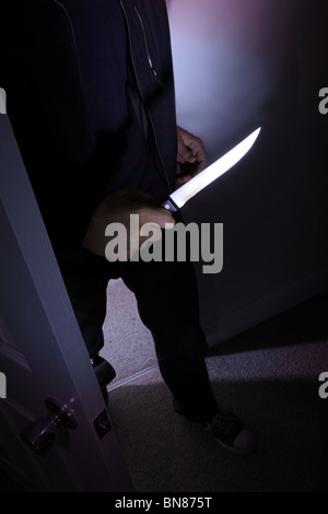 Dark figure of a man entering a room holding a knife. Stock Photo