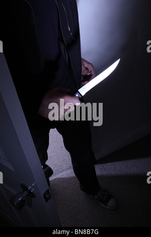 Dark figure of a man entering a room holding a knife. Stock Photo