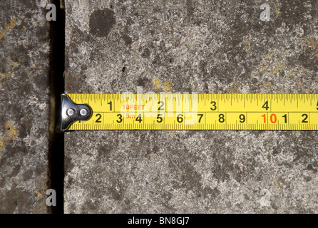 A tape measure showing inches and centimeters is shown measuring a concrete slab. Stock Photo