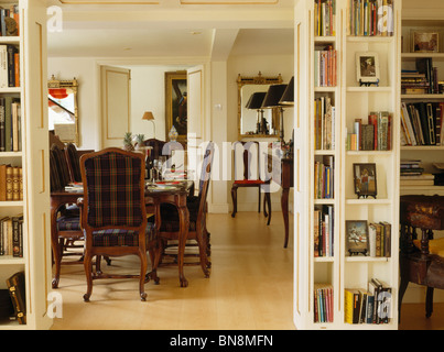 Shelves on either side of open double doors to dining room with tartan upholstered chairs and wooden flooring Stock Photo