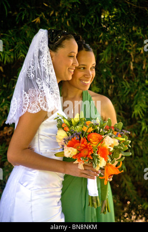 Mixed-race bride and her bridesmaid proudly pose with their flowers before a formal outdoor wedding in Orange, CA. MODEL RELEASE Stock Photo