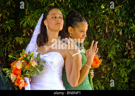 A mixed-race bride and her bridesmaid proudly pose with their flowers before formal outdoor wedding in Orange, CA. MODEL RELEASE Stock Photo