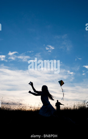 Young Girl and adult having fun flying a kite in the English countryside. Silhouette Stock Photo