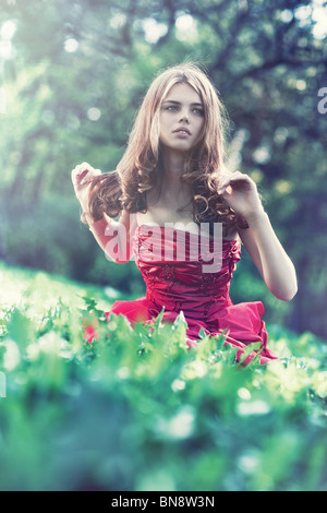 Young woman in red dress sitting on grass and looking aside.