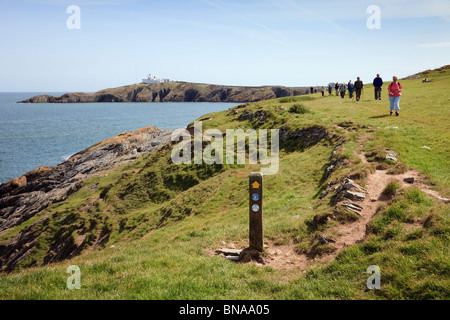 Isle of Anglesey Coastal Footpath and Wales Coast Path waymarker with people walking from Point Lynas. Llaneilian Isle of Anglesey North Wales UK Stock Photo