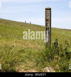 South West Coast path waymarker at Henna cliff near Morwenstow Cornwall with two distant walkers climbing the hill Stock Photo