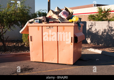 An orange dumpster is full of various types of trash and ready to be emptied. Stock Photo