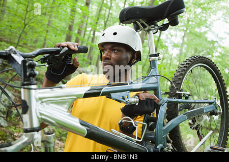 Male cyclist carrying bike in forest Stock Photo