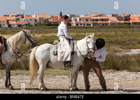 young female gardian, cowgirl of the Camargue region, on her horse, cowboy helping with the horses bridle Stock Photo