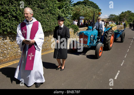 A priest leads a funeral procession in the English village of Falmer, Sussex. The coffin is on the trailer of a tractor. Stock Photo