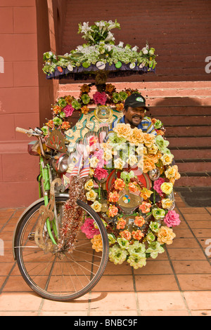 Rickshaw in Melaka, decorated with plastic flowers, and his smiling driver sat on passenger seat waiter for customers Stock Photo
