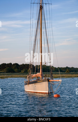 Grey hull old gaff rigged sailing boat moored to bouy in a quiet river surrounded by fields and trees Stock Photo