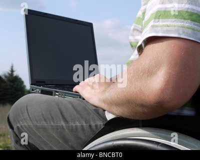 Handicapped man on wheelchair using laptop outdoors Stock Photo