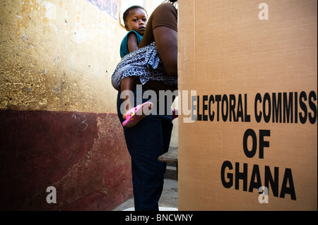 A woman carrying her child on her back votes in a booth during presidential and parliamentary elections in Accra, Ghana Stock Photo