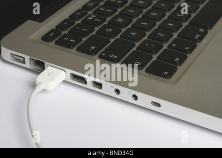 Close up of white iPod USB cable plugged into computer I/O ports on the side of a Aluminum Apple Macbook Stock Photo