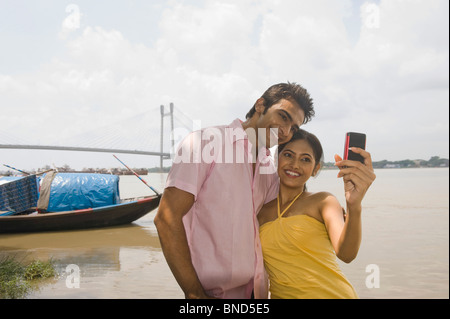 Couple taking picture of themselves with bridge in the background, Vidyasagar Setu, Hooghly River, Kolkata, West Bengal, India Stock Photo