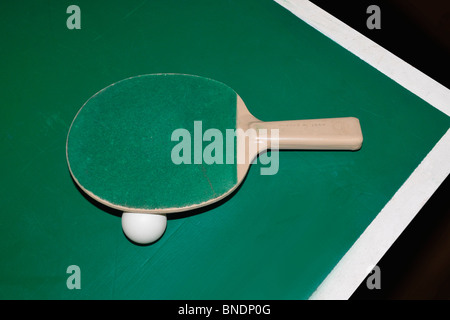 A table tennis bat and ball sit on the edge of a table tennis table. Stock Photo