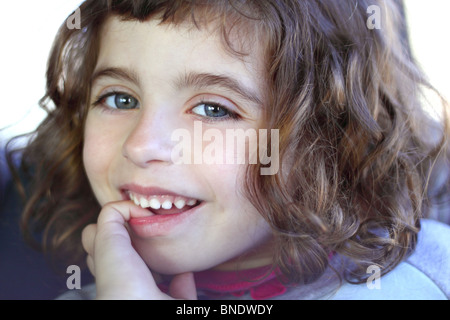 little girl smiling shy biting finger blue eyes Stock Photo