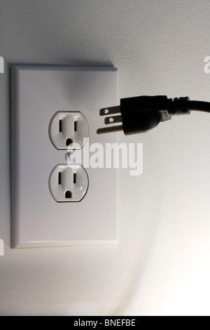 American Three Pronged Plug hovering in front of a 110 Volt A/C Electrical Outlet Stock Photo