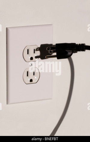 American Three Pronged Plug with shadow hovering in front of a 110 Volt Electrical Outlet. Stock Photo