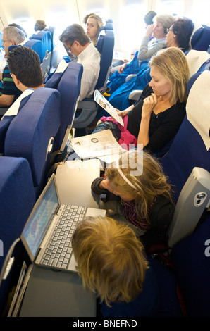 Brother and Sister watching film on laptop in plane while mother relaxing in Netherlands, Europe Stock Photo