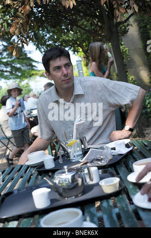 Middle-aged man at outdoor cafe sitting at a table with tea trays he is iistening to a conversation and looks serious Stock Photo