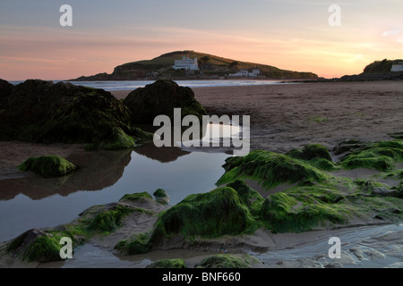 Bigbury-on-Sea and Burgh Island at sunset, South Hams, Devon. Low tide reveals seaweed covered rocks on the beach. Stock Photo