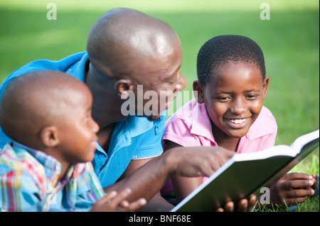 Father reading with children (4-8) on lawn in garden, Johannesburg, Gauteng Province, South Africa Stock Photo