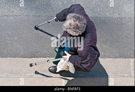 Elderly woman with caliper sticks walking alongside pavement - France. Stock Photo