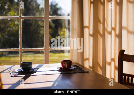 Two cups of tea or coffee on a table in the early morning sun. Backlit. Stock Photo