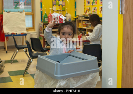 4 year old Spanish preschool girl throwing away an empty container of milk in to a garbage can Stock Photo