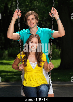 Young happy couple in their early thirties having fun on a swing at children's playground Stock Photo