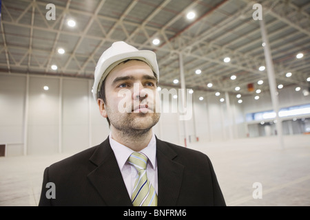 Businessman in hard hat stands in brightly lit warehouse Stock Photo